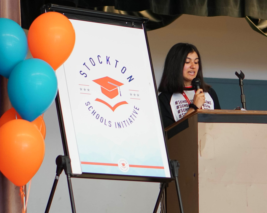 Sahila Shah speaks at a podium next to a sign that says ‘Stockton Schools Initiative’