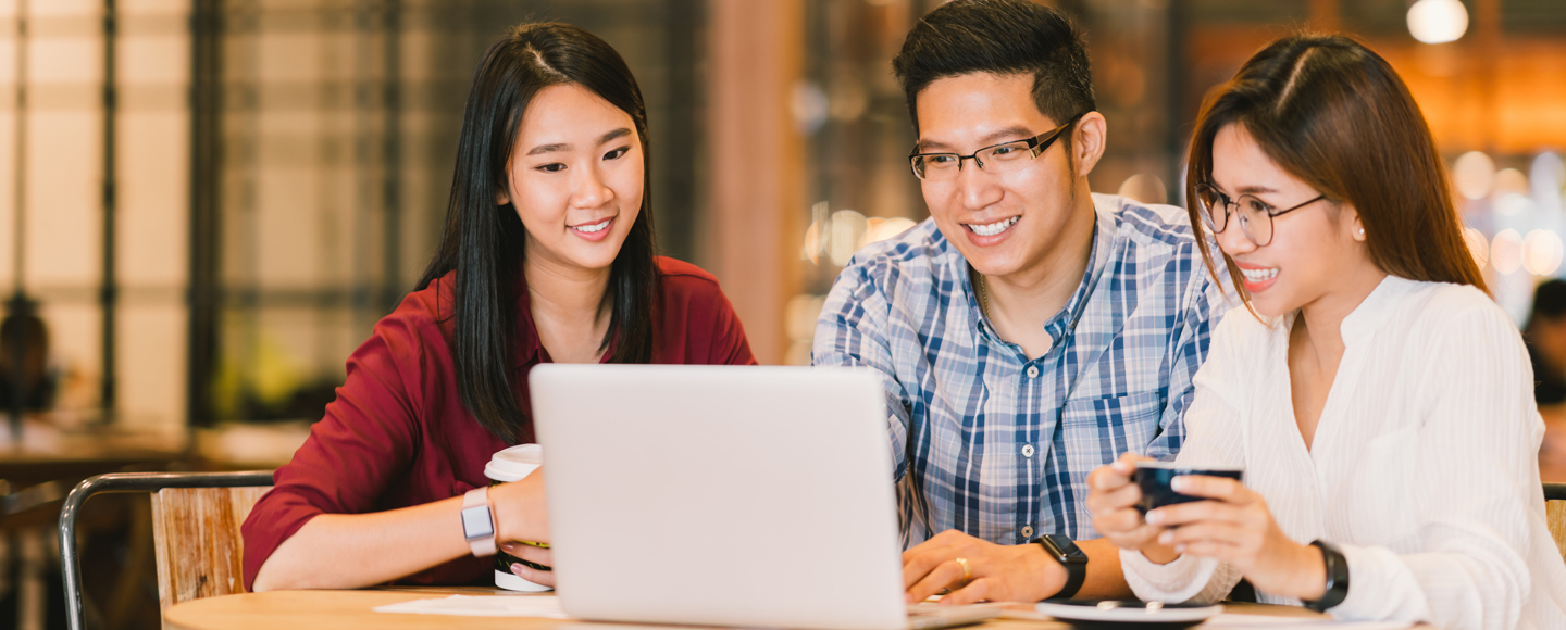 Three young adults are sitting around a laptop and smiling.