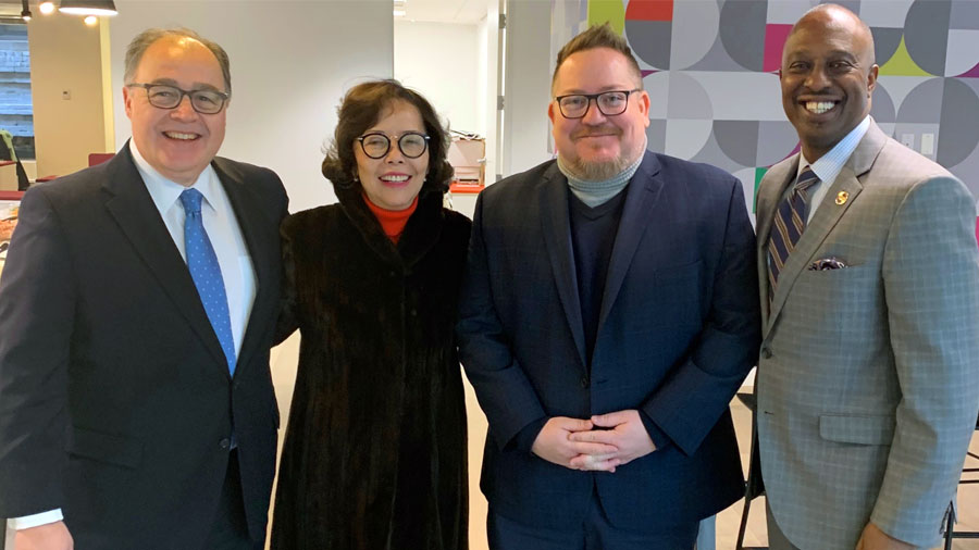 A group of three men and a woman stand together and smile at the camera.