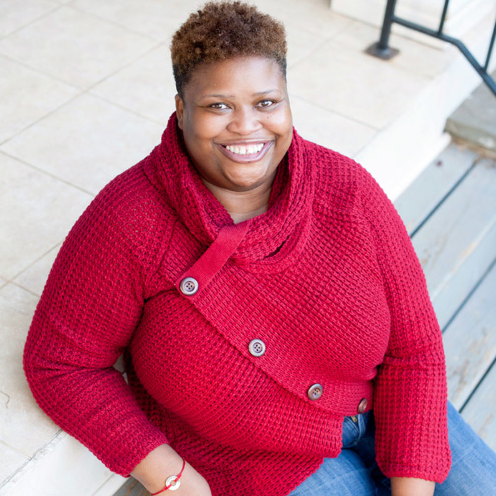 Ruby Taylor sits smiling at the camera, wearing a red sweater and jeans.