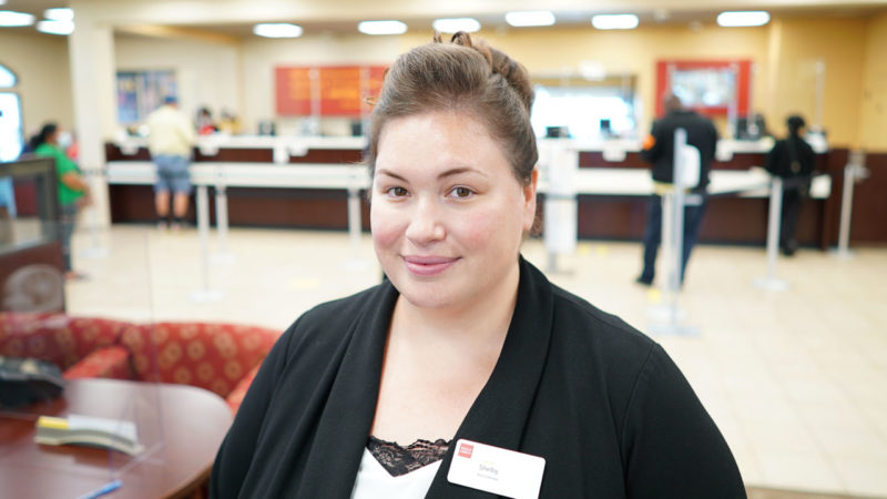 A woman stands inside a bank branch and smiles.