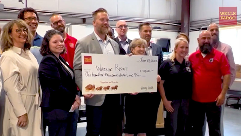 A group of people stand together around a large check made out to Warrior Rising.