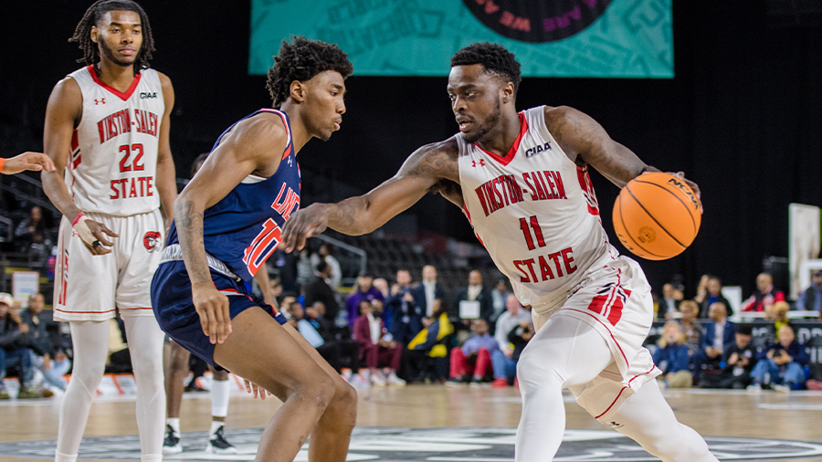 A college basketball player is being guarded by an opposing player as he tries to dribble past him.