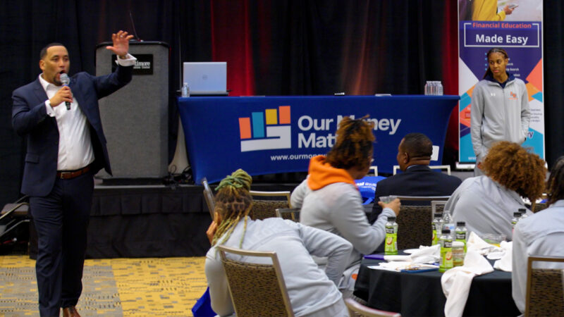 A man with a microphone speaks to students in a room.