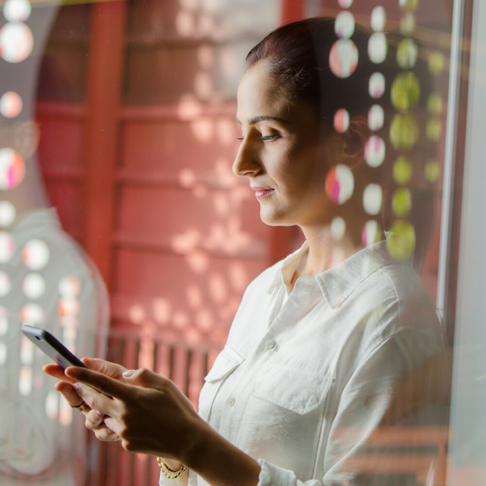 A woman is looking down at a cell phone that she is holding with both hands.