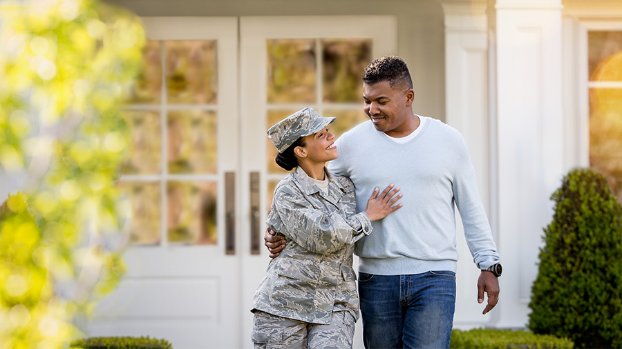 A woman in military uniform hugs her significant other as they stand outside their home.