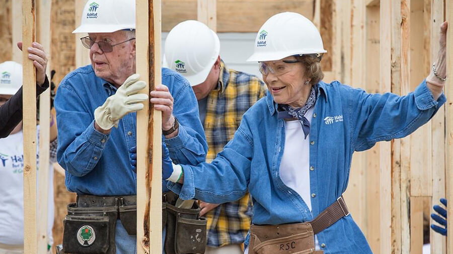 Jimmy and Rosalynn Carter wearing safety hats and tool belts on a construction site.