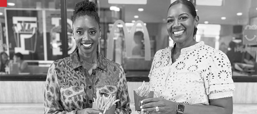 Two women hold boxes of fries in front of a McDonald's restaurant.