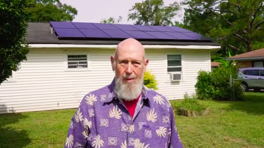 Marc Thomas stands in front of his house which has solar panels on the roof.